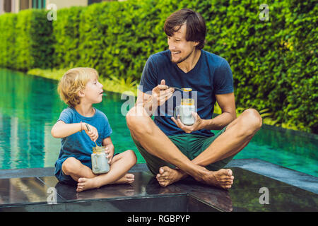 Père et fils manger le dessert avec chia seeds et de mangues à la piscine le matin. la saine alimentation, l'alimentation, les régimes végétariens et personnes concept Banque D'Images