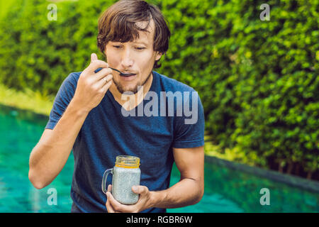 L'homme manger le dessert avec chia seeds et de mangues à la piscine le matin. la saine alimentation, l'alimentation, les régimes végétariens et personnes concept Banque D'Images