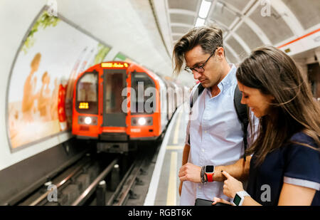 UK, Londres, couple en attente à la station de métro à la plate-forme à smartwatch Banque D'Images