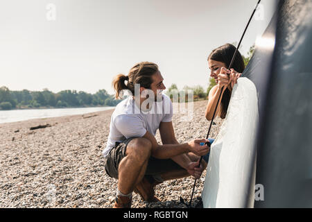 Smiling young couple mise en place d'une tente au bord du fleuve Banque D'Images