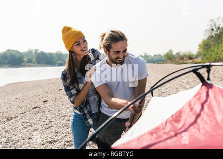 Happy young couple mise en place d'une tente au bord du fleuve Banque D'Images