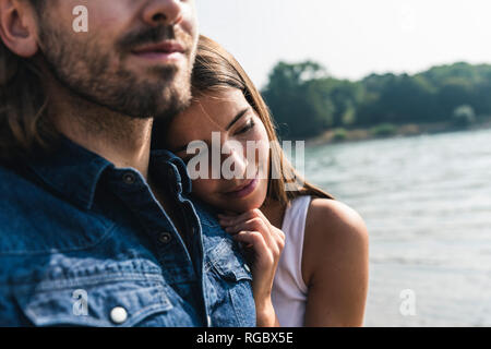 Souriante jeune femme appuyée contre l'épaule de l'homme au bord de la rivière Banque D'Images