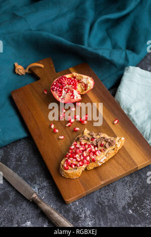 Tranche de pain avec du beurre d'arachides, graines de grenade et de morceaux de chocolat sur planche de bois Banque D'Images