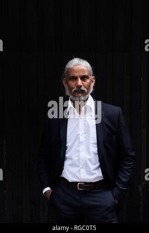 Portrait de senior businessman élégant avec des cheveux gris et sa barbe debout sur un fond sombre Banque D'Images