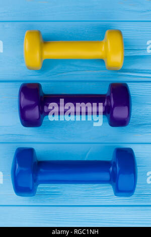 Trois haltères colorés sur fond de bois. Jaune, violet et bleu sur bleu haltères surface du bois. Sport et fitness concept. Banque D'Images