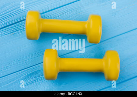 Haltères en bois jaune sur fond bleu. L'équipement de remise en forme sur des planches en couleur. Sport et mode de vie sain. Banque D'Images