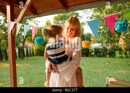 Heureuse mère portant sa fille sur un jardin d'anniversaire Banque D'Images