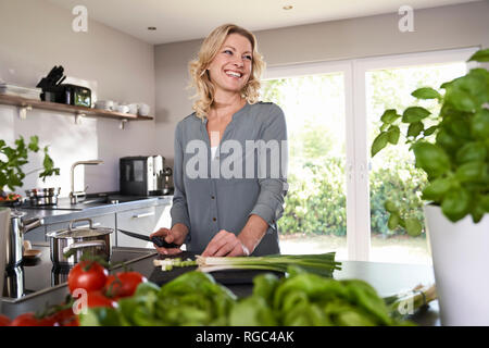 Smiling woman cutting oignons de printemps dans la cuisine Banque D'Images