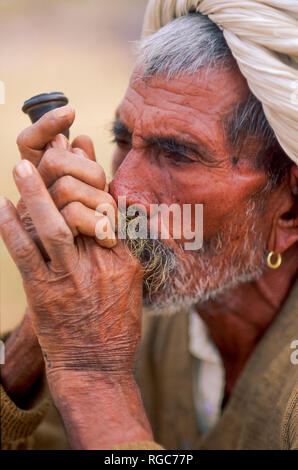 Close-up of a senior man rajasthani fumant une pipe, le port d'oreille et d'un turban blanc, Camel juste à Pushkar, Rajasthan, India Banque D'Images