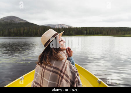 La Finlande, Laponie, heureuse femme portant un chapeau sur un bateau sur un lac Banque D'Images