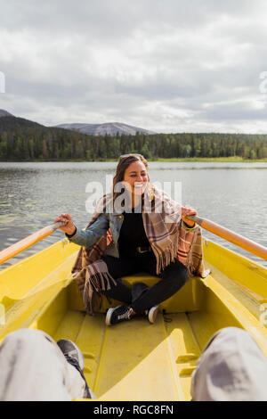 La Finlande, Laponie, riant femme portant une couverture dans une barque sur un lac Banque D'Images