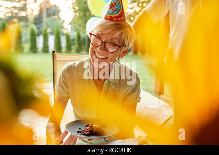 Smiling mature woman holding plaque à gâteau sur un anniversaire garden party Banque D'Images