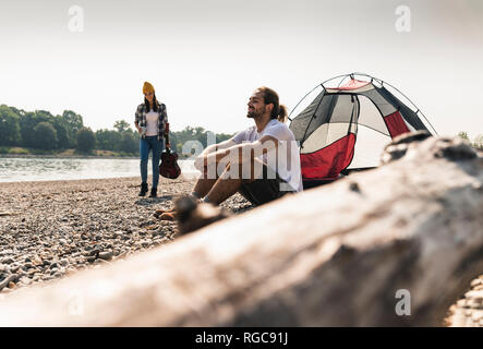 Couple au bord de la rivière avec guitare et tente Banque D'Images