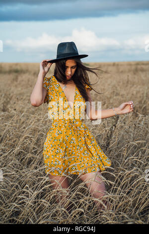 Jeune femme portant tenue d'été avec des fleurs et un chapeau de danser dans un champ de maïs Banque D'Images