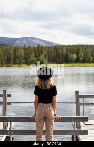 La Finlande, Laponie, femme portant un hat standing on jetty sur un lac Banque D'Images