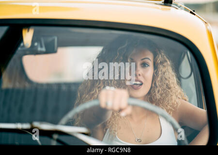 Portrait de femme blonde surpris au volant voiture classique Banque D'Images