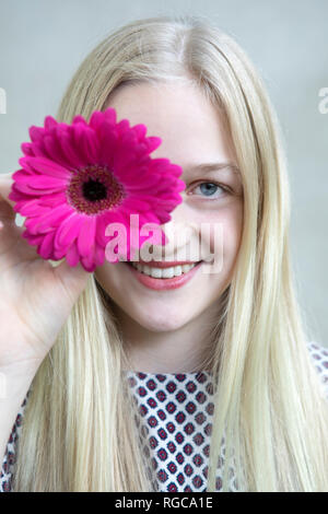 Portrait of smiling blonde avec fleur de Gerbera rose Banque D'Images