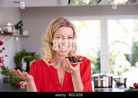 Femme exubérante using smartphone in kitchen Banque D'Images