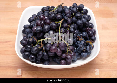 La nature morte avec beaucoup de vin mûr avec des grappes de petits fruits noirs dans square bowl sur fond blanc en bois close up Banque D'Images