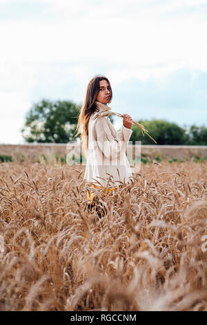 Young woman wearing oversized Pull col roulé debout dans un champ de maïs Banque D'Images