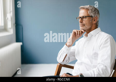 Manager sitting in chair dans son bureau, regardant par la fenêtre, pensant Banque D'Images