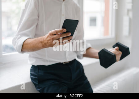 Succès manager à l'aide du smartphone et l'entraînement avec un haltère Banque D'Images