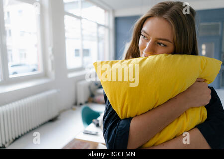 Smiling young businesswoman avec oreiller jaune in office Banque D'Images
