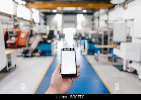 Hand holding Smartphone avec écran vide dans un atelier d'usine Banque D'Images