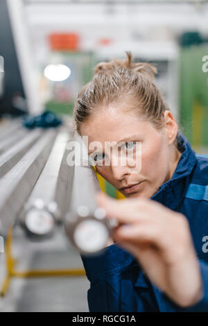 Jeune femme travaillant à titre de travailleur qualifié dans une entreprise de haute technologie, contrôle des tiges d'acier Banque D'Images