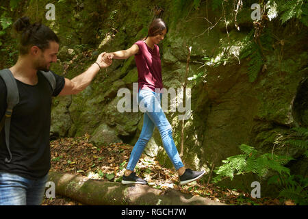 Espagne, Canaries, La Palma, smiling man holding part de votre petite amie sur tronc d'arbre d'équilibrage Banque D'Images