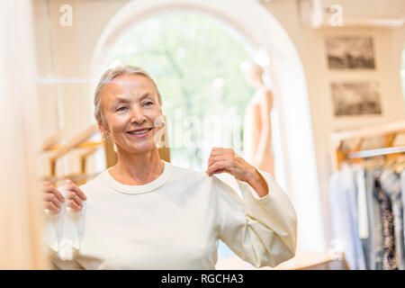 Smiling senior woman trying on pull dans une boutique Banque D'Images