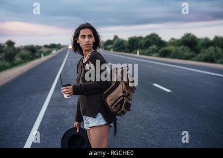 Portrait de jeune femme de l'auto-stop et sac à dos avec boissons debout sur lane