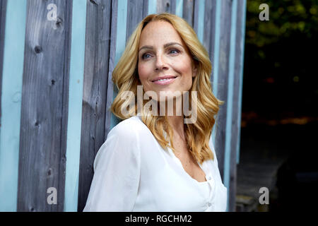 Smiling blonde woman in front of wooden wall Banque D'Images