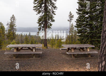 Deux tables en bois picknic à une zone de visualisation avec Diamond Lake dans la distance sur un après-midi brumeux dans l'Oregon. Banque D'Images