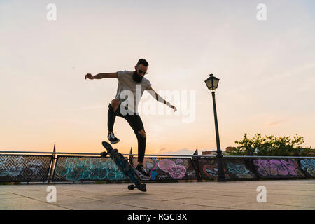 Jeune homme faisant un tour de planche à roulettes dans la ville au coucher du soleil Banque D'Images