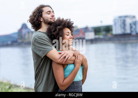 Germany, Cologne, young couple hugging at the riverside Banque D'Images