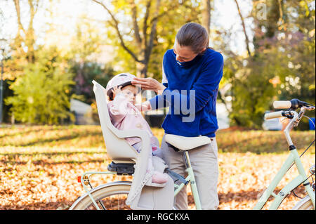 Mère et fille riding bicycle, baby wearing helmet assis dans le siège pour enfants Banque D'Images