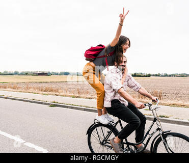 Happy young couple riding ensemble sur un vélo sur route de campagne Banque D'Images