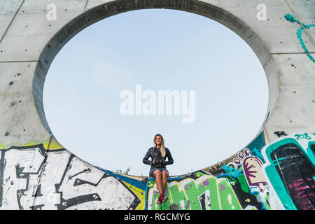 Jeune femme assise dans un grand trou dans un mur de béton Banque D'Images