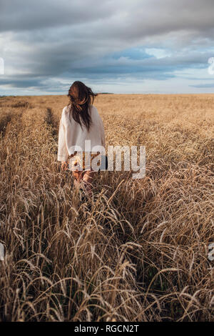 Vue arrière de young woman walking in corn field Banque D'Images