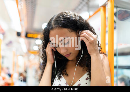Jeune femme à l'écoute de la musique avec des écouteurs sur la rame de métro Banque D'Images