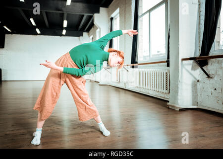 Les agréable aux cheveux rouges professeur de yoga dans un col roulé faisant office Banque D'Images