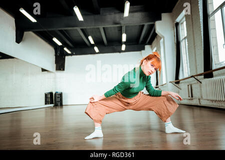 Beau slim coach de yoga dans un col roulé vert faisant des pattes d'asanas Banque D'Images