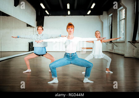 Belle Slim professeur de ballet faisant s'accroupir avec deux jeunes étudiants Banque D'Images