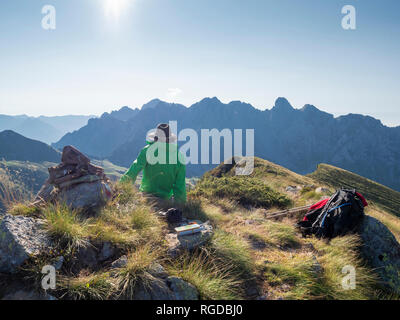 L'Italie, Lombardie, Préalpes Bergamasque, randonneur assis sur viewpoint de Monte Gardena, Cima Bagozza contre le soleil Banque D'Images