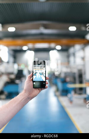 Hand holding smartphone dans un atelier d'usine Banque D'Images