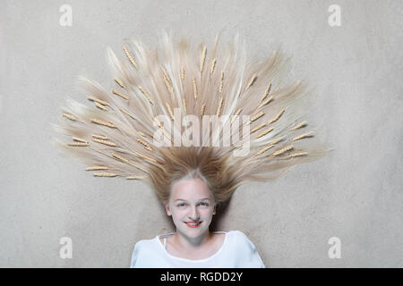 Portrait of smiling girl lying on floor avec des épis de blé sur les cheveux Banque D'Images