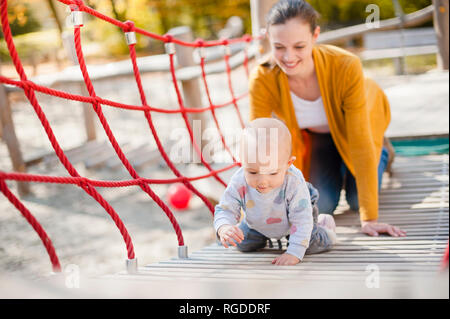 Mère regardant son bébé fille jouant sur l'aire de jeux Banque D'Images