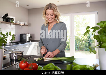 Smiling woman cutting oignons de printemps dans la cuisine Banque D'Images