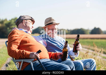 Deux vieux amis assis dans les champs, la consommation de bière, en parlant de vieux temps Banque D'Images